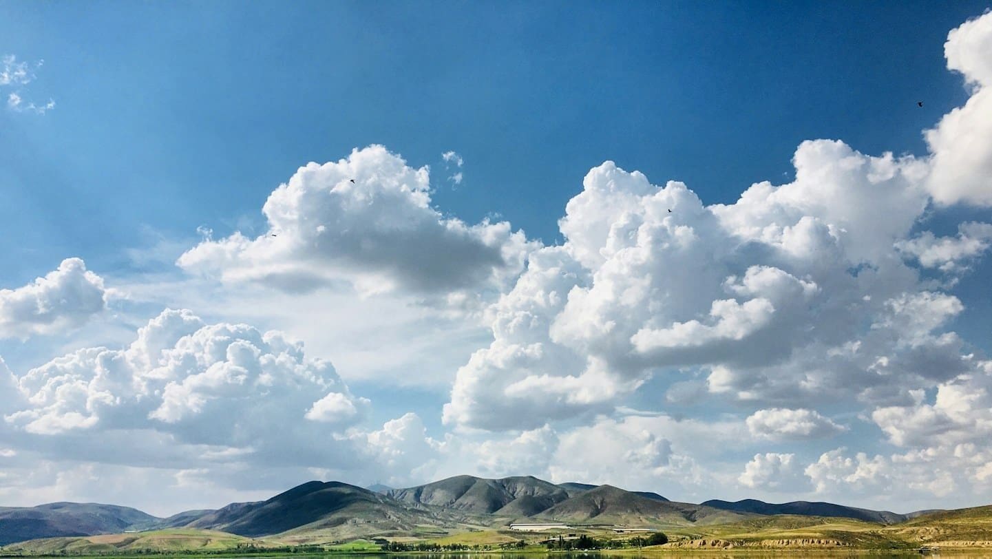 green grass field near lake under white clouds and blue sky during daytime