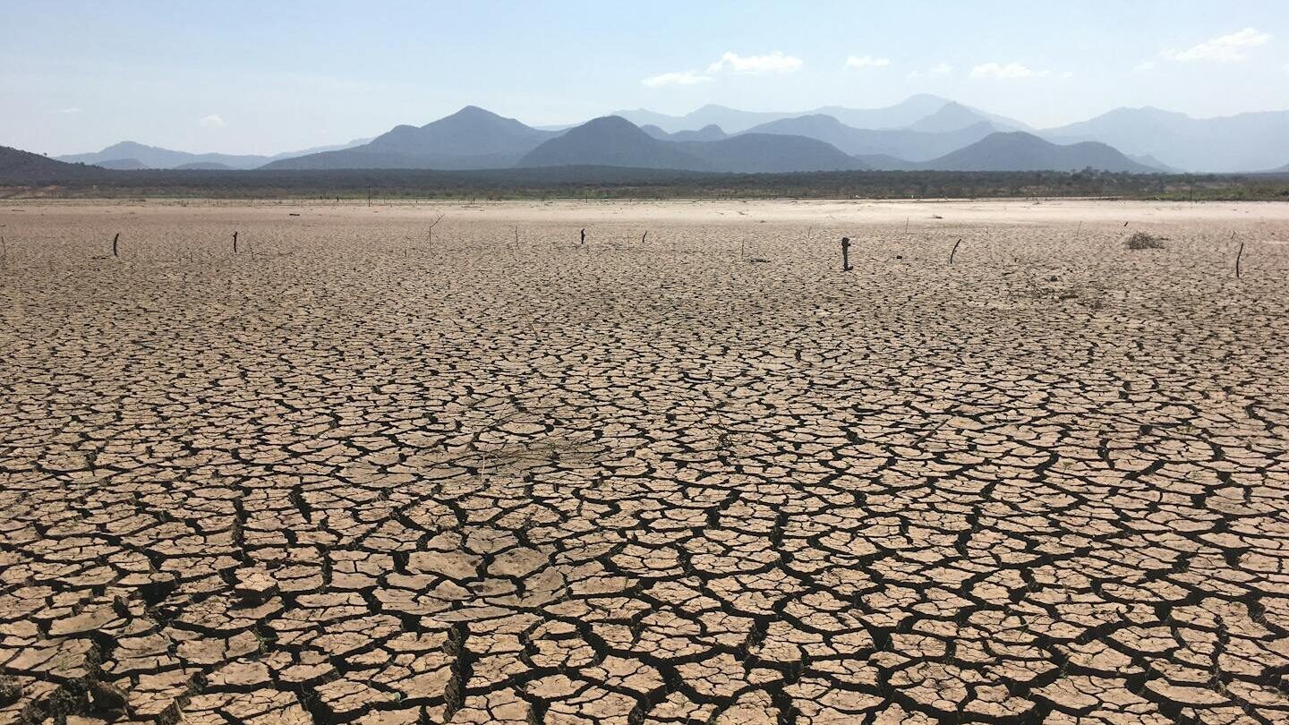 A vast, cracked earth landscape under clear skies depicting severe drought conditions.