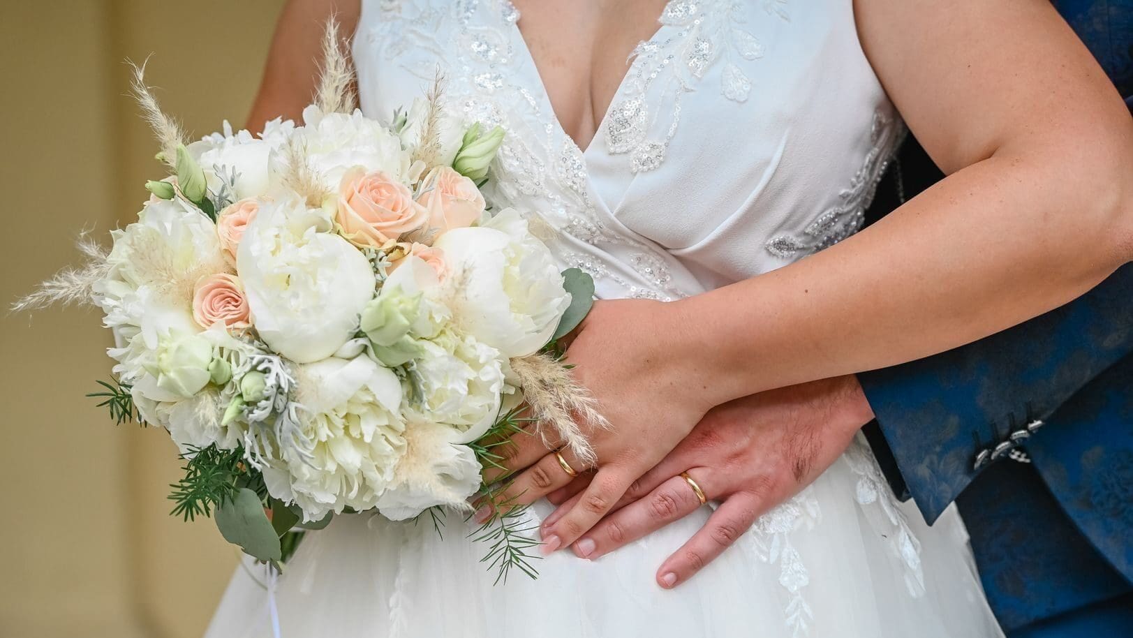 Close-up of bride and groom with elegant bouquet, showcasing wedding rings in an intimate pose.